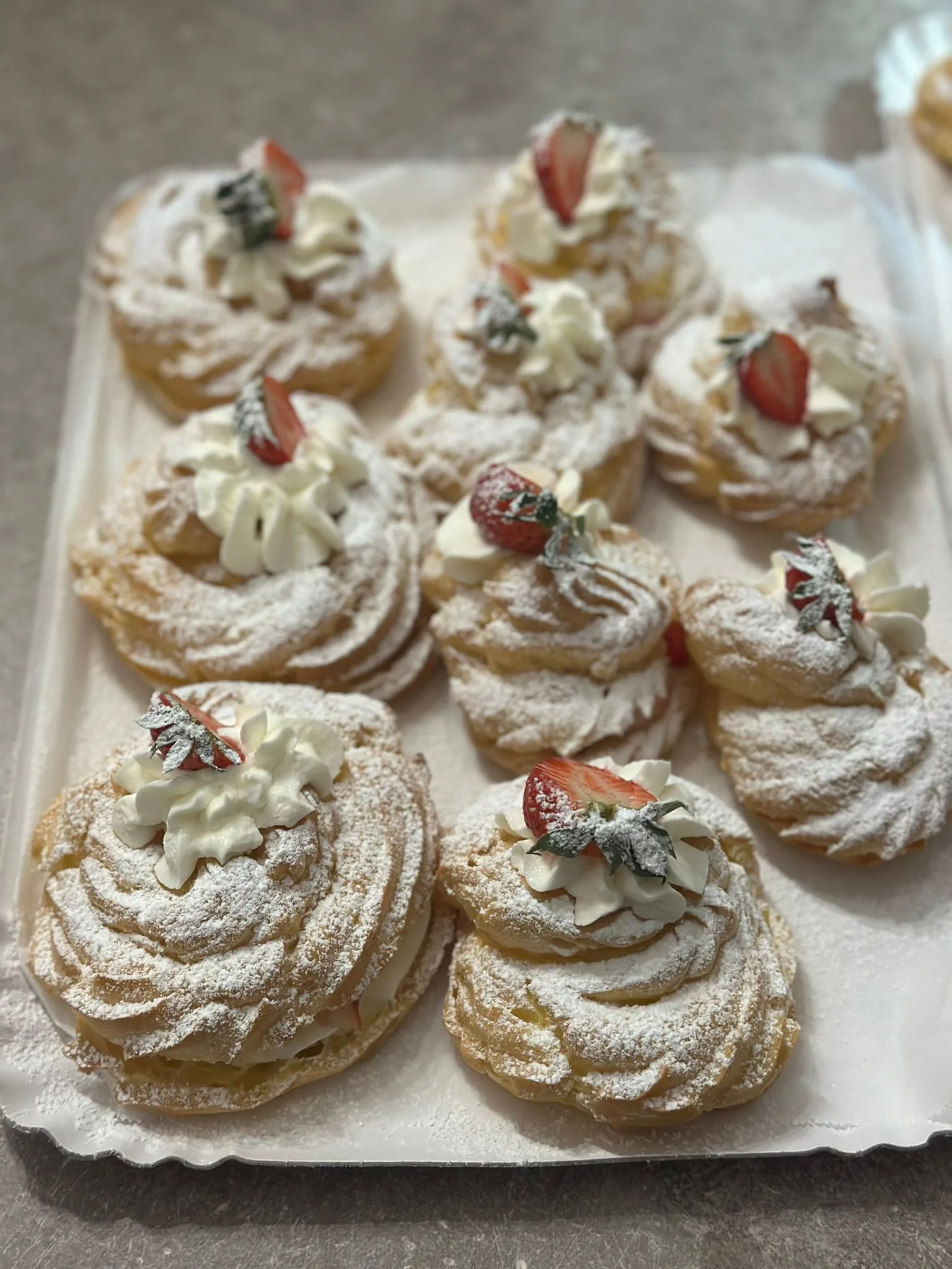 Inquadratura dall'alto di un vassoio con zeppole di San Giuseppe farcite con crema di panna e mascarpone, zucchero a velo e decorate con fragole fresche tagliate a metà.