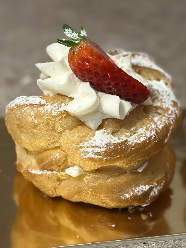 Bignè grande di pasta choux farciti con panna montata, spolverati di zucchero a velo e decorati con fragole fresche su un vassoio dorato.