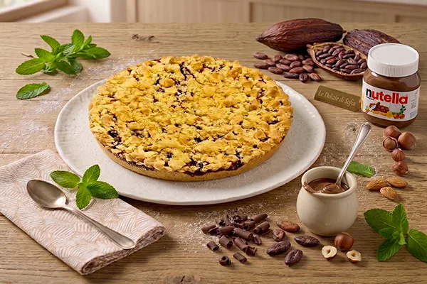 Sbriciolata artigianale alla Nutella del Laboratorio Le Delizie di Sofia servita su un piatto con ingredienti di decorazione come nocciole intere e fave di cacao.
