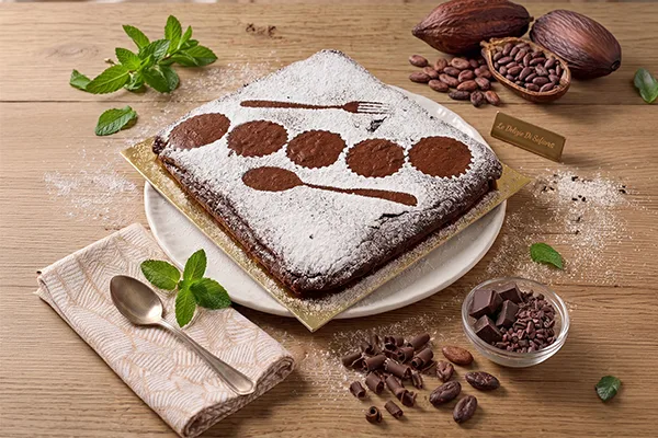 Torta Tenerina artigianale al cioccolato fondente Le Delizie di Sofia, spolverata con zucchero a velo e cacao, disposta su un'alzatina con fave di cacao decorative.